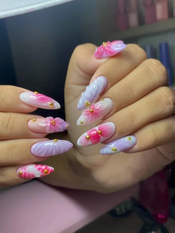 Long almond-shaped nails with a watercolour effect, featuring soft pink and lavender floral designs and gold bead accents.