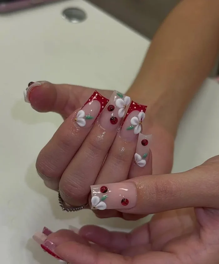 Charming summer nails with red polka dot French tips on long square nails, detailed with 3D white flowers and cute ladybugs.