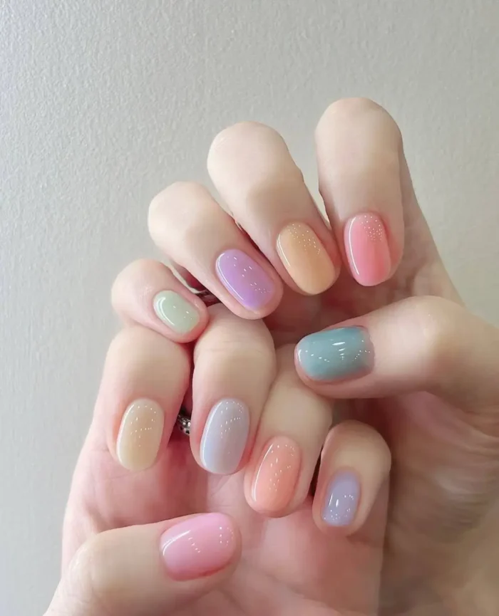 Cute simple gel manicure with a mix of sheer pastel rainbow sherbet colors, some with subtle shimmer, on short rounded nails.