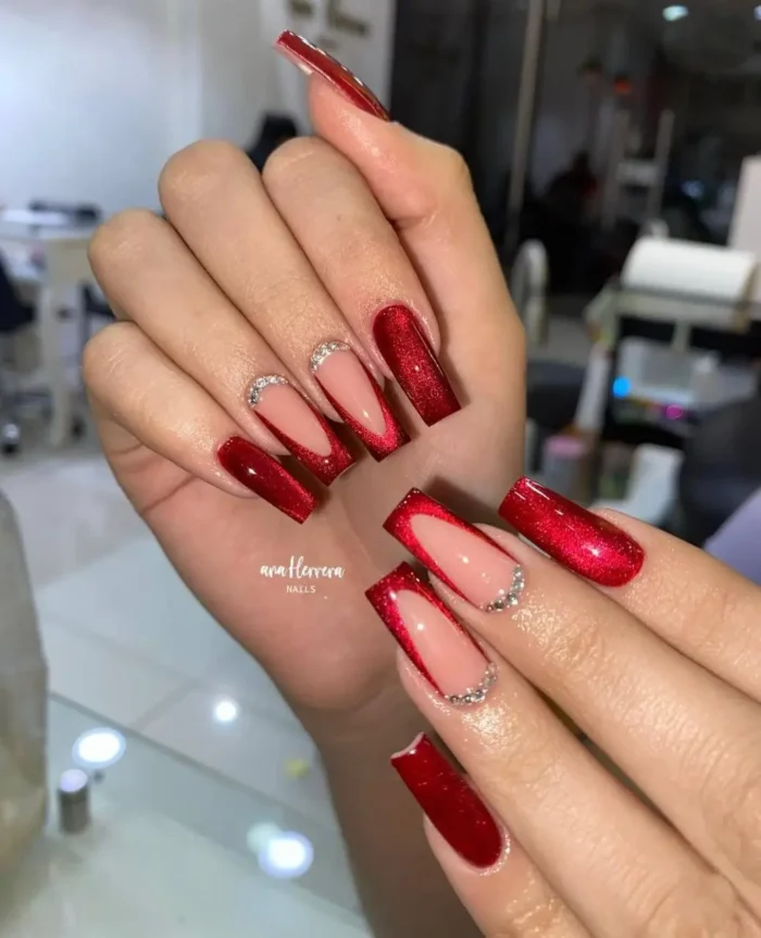 A glamorous red nail design on long square nails, featuring a cat-eye polish V-tip and a rhinestone accent line.
