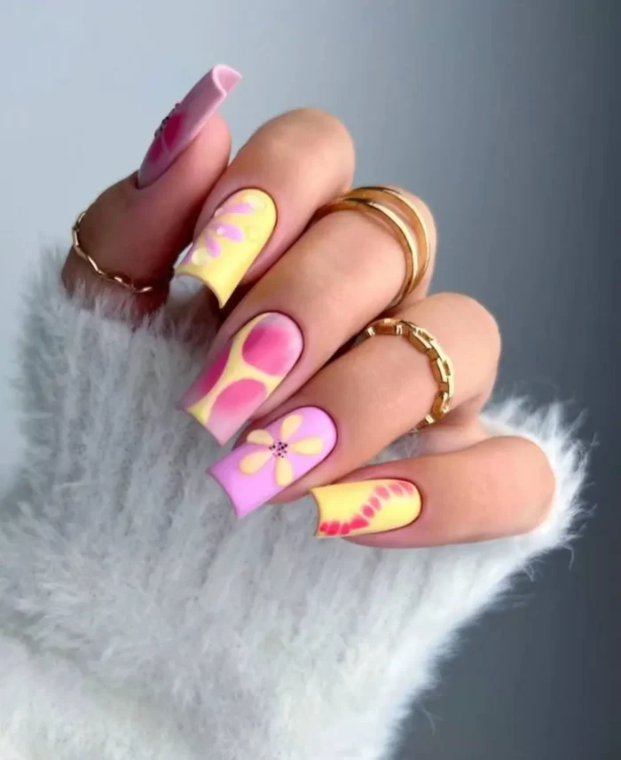 A vibrant manicure on long square nails featuring a mix of butter yellow and pink abstract designs and floral art.