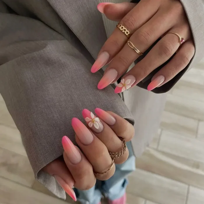 Long almond-shaped nails with a pink to nude ombré effect, accented with a white 3D flower.