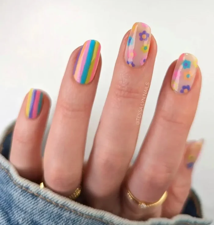 A cheerful and cute nail idea with a '70s-inspired design of vibrant rainbow stripes and simple daisy floral art.