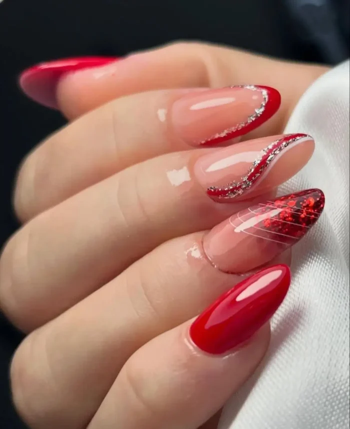 An intricate red nail design featuring a mix of solid red, red glitter French tips, and silver glitter accents.