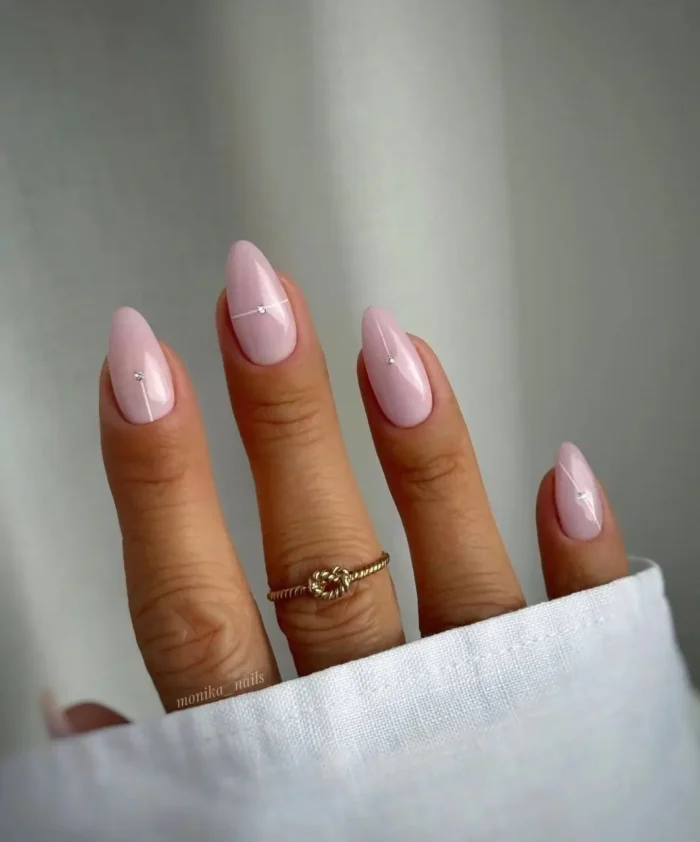 Medium almond nails in soft baby pink, each featuring a sleek vertical silver line accented by two tiny, sparkling rhinestones.