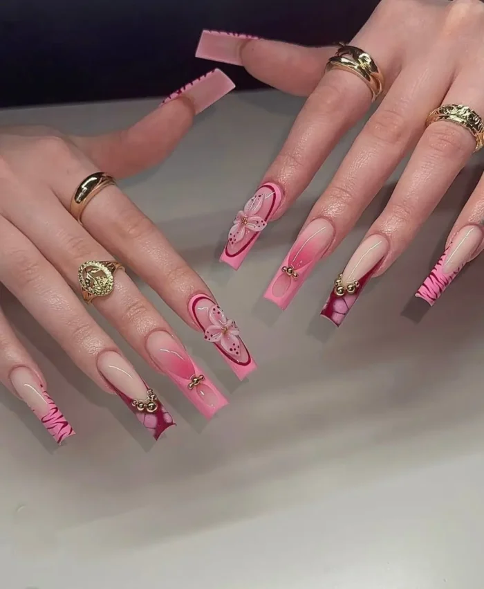 Elegant long square pink nails for summer with an airbrushed ombre effect, delicate 3D flowers, and gold bead details.