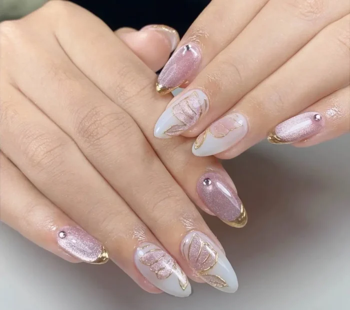 Almond nails alternating between shimmery pink with gold tips and rhinestones, and a milky base with delicate gold botanical leaf outlines.