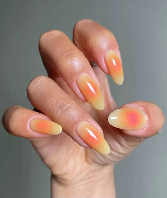 A close-up of almond-shaped nails with a butter yellow and peach-orange aura ombre effect, resembling a sunrise.