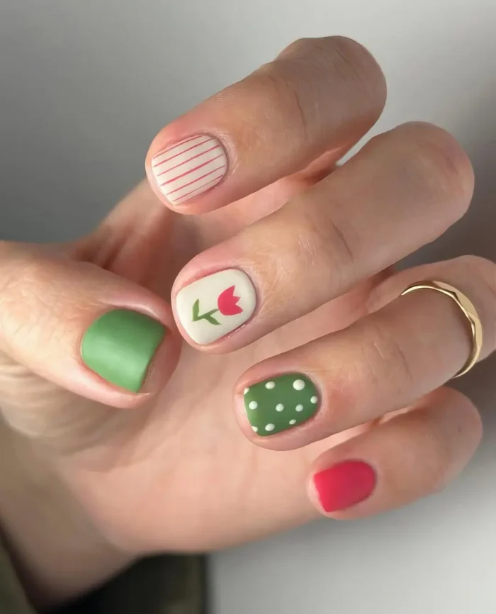 Short square nails with a matte finish featuring a mixed pattern design: coral stripes, a tulip drawing, green with polka dots, and solid colors.