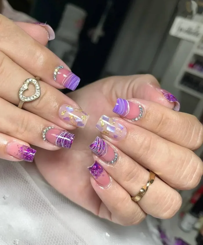 Short square nails with a petite plum sparkle purple nail design, featuring chunky glitter, gold foil, and rhinestone accents.