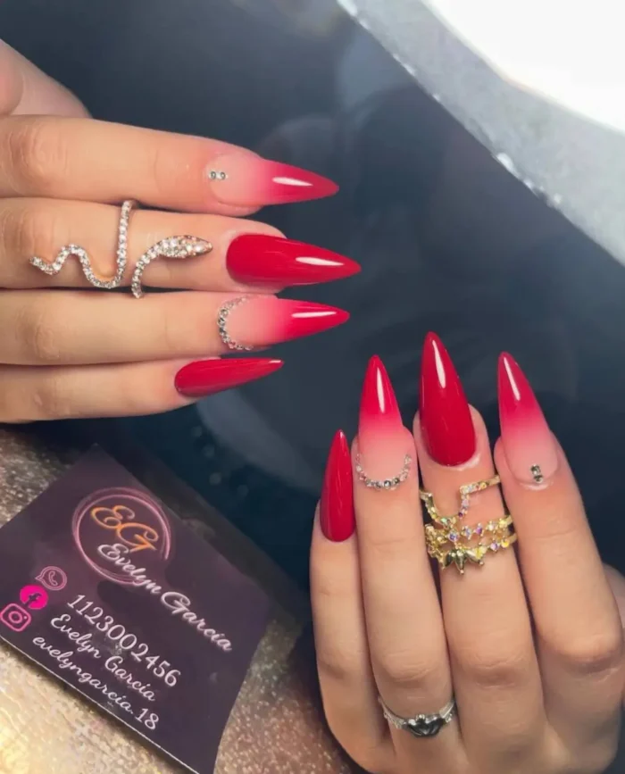 A dramatic red ombré nail design on long stiletto nails, accented with sparkling rhinestone details.