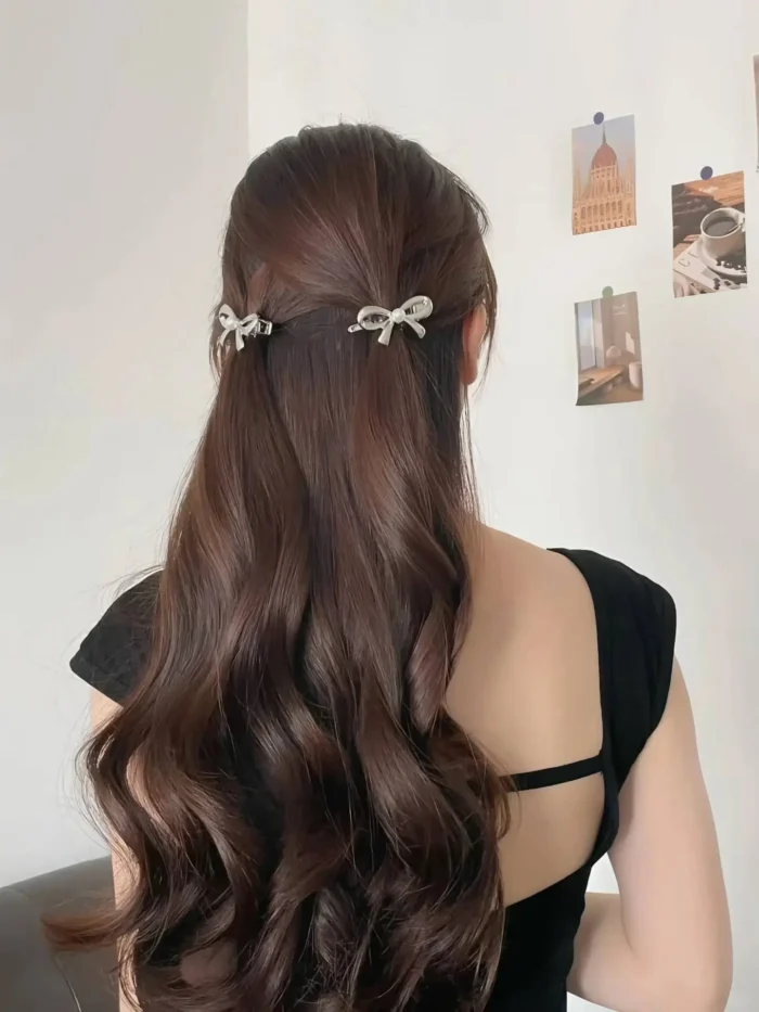 Rear view of a simple half-up style on dark wavy hair, held in place by two small, symmetrical silver bow clips.