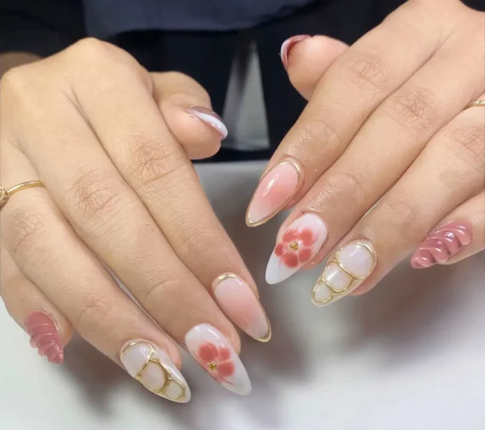 Long almond nails with mixed designs including pink florals on white ombre, gold wire patterns, sculpted pink waves, and gold French tips.
