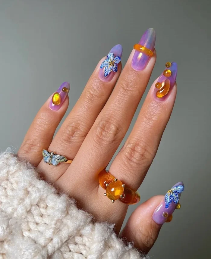 Mystical summer nail art on long almond nails with a purple and orange aura effect, detailed 3D butterflies, and amber gem accents.