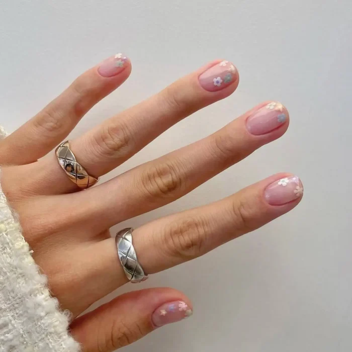 Very short, natural nails with a sheer glossy finish, adorned with tiny minimalist pastel flower details.
