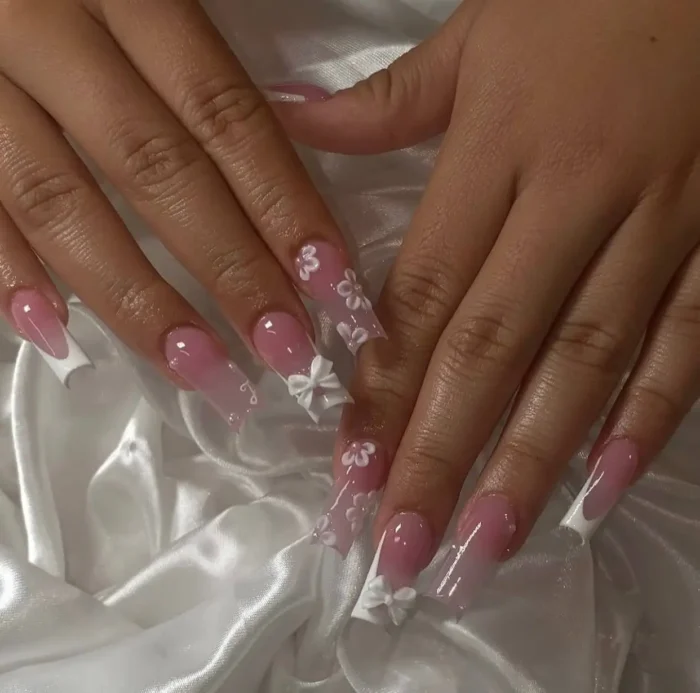 Long nails with classic white French tips, adorned with delicate 3D white bows and translucent white floral details.