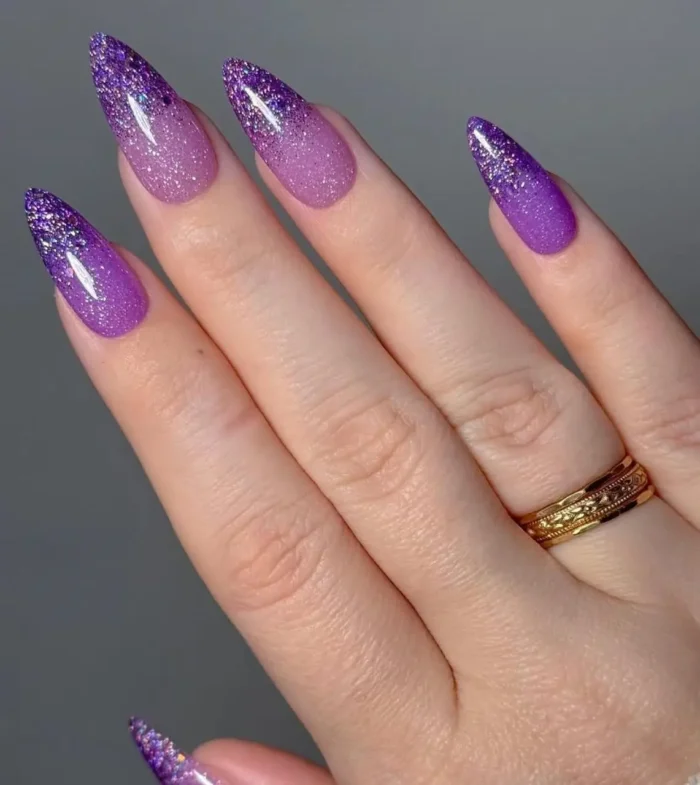 Long almond nails with a stardust purple gradient nail design, showcasing rich purple glitter fading to a softer shimmer.