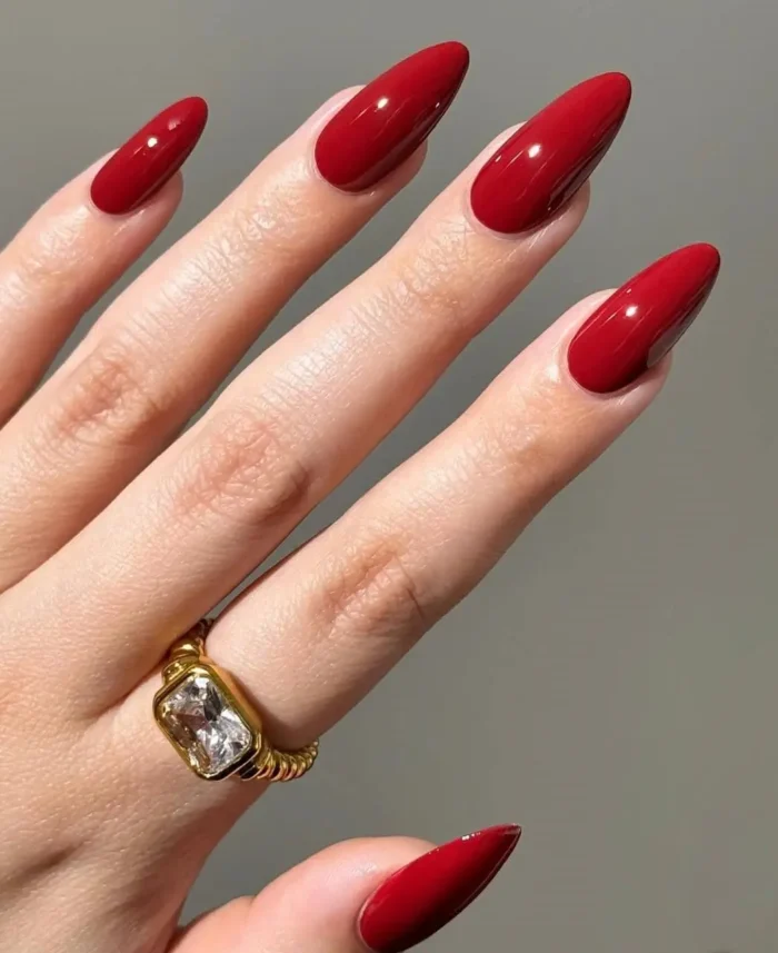 A close-up of long, almond-shaped nails with a flawless, high-gloss classic red manicure.