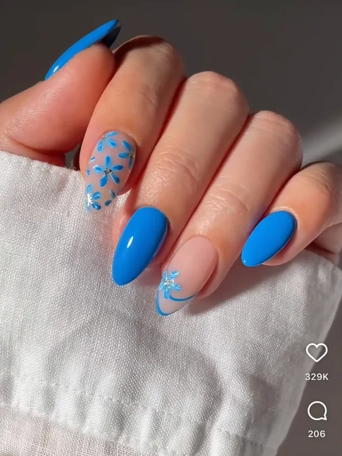 Chic almond nails with modern blue floral art, featuring bold cornflower blue polish and a negative space design with scattered blossoms.
