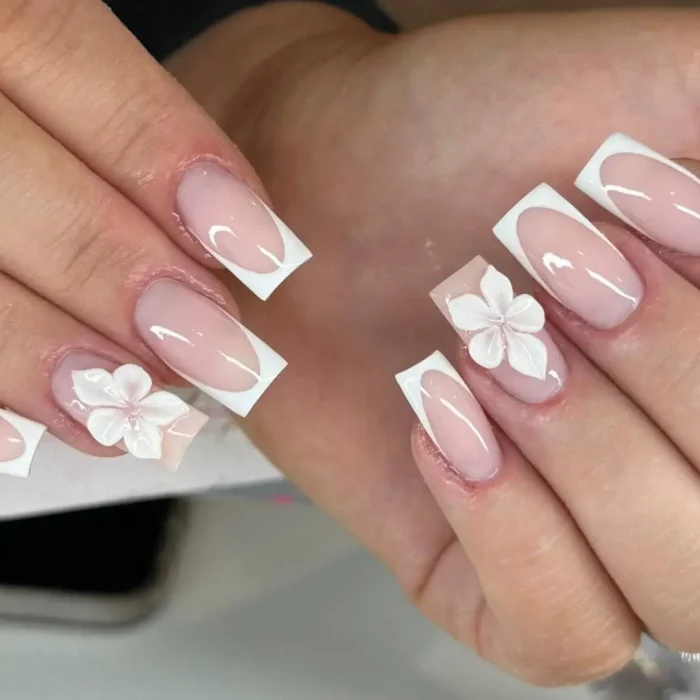 A modern French manicure with a deep white tip and a delicate 3D white flower on an accent nail.