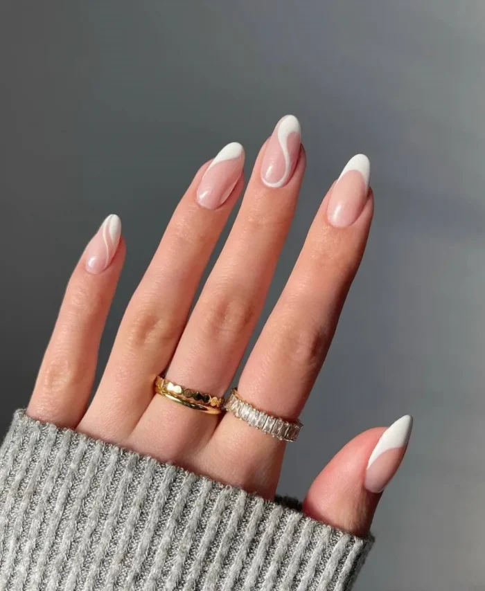 Modern French tip nails with a natural nude base and elegant white swirling lines on almond shapes.