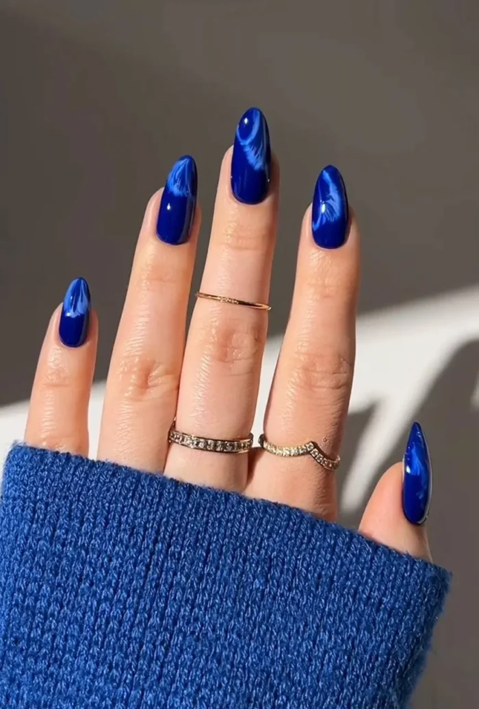 A close-up of long almond nails with a glossy cobalt blue and white smoke effect nail art design.
