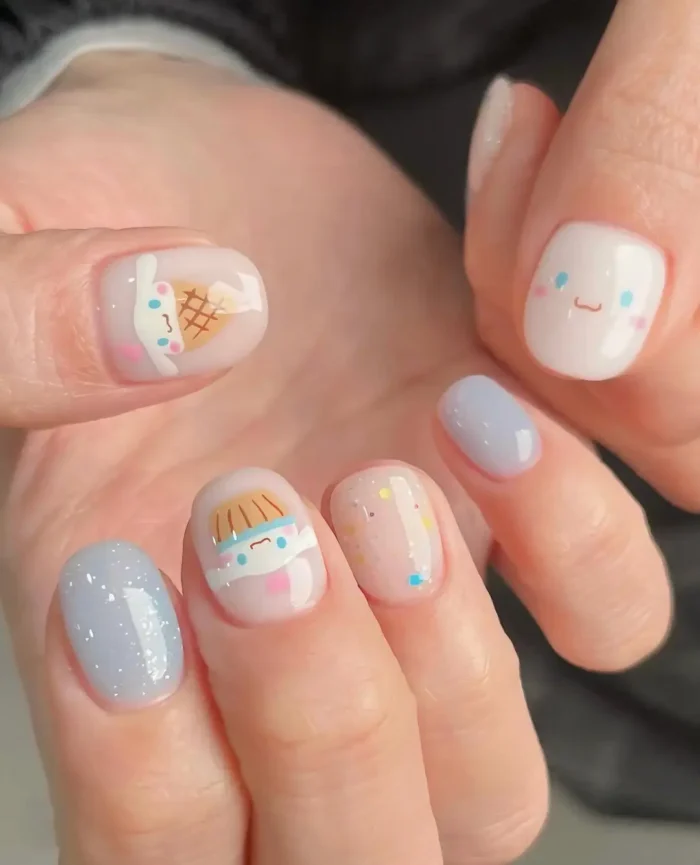 Very short rounded nails with a cute kawaii theme featuring pastel blue glitter, illustrated characters, and confetti glitter on milky and sheer bases.