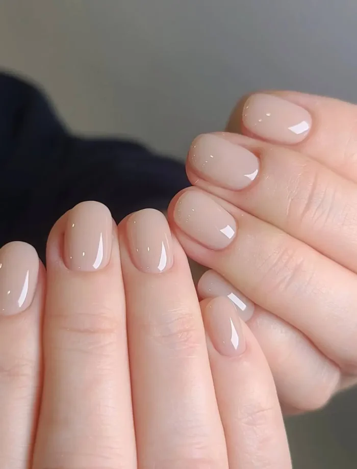 Cute simple gel manicure with a sheer natural nude pink base and very subtle sparse glitter on very short rounded nails.
