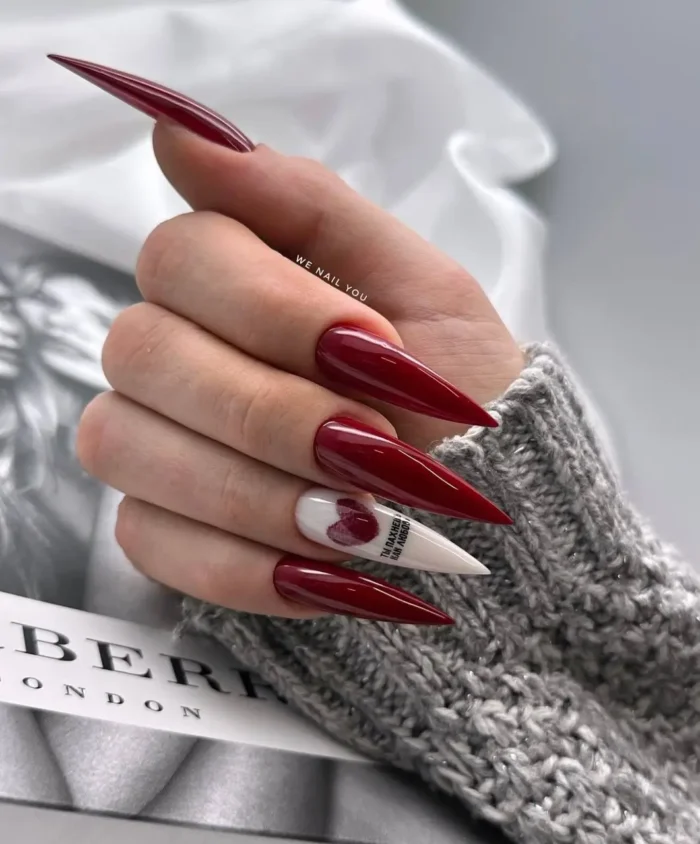 A dramatic red stiletto manicure with a single white accent nail featuring a red wax seal design.