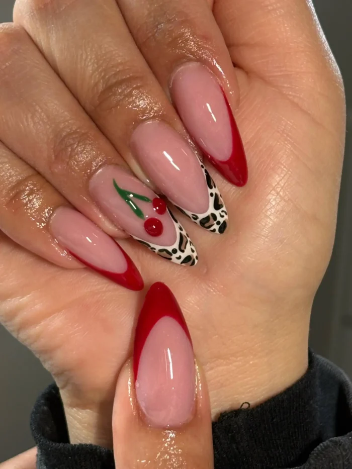 Almond-shaped nails with a mix of designs including red V-French tips, leopard print V-French tips, and hand-painted cherry accents on a sheer pink base.