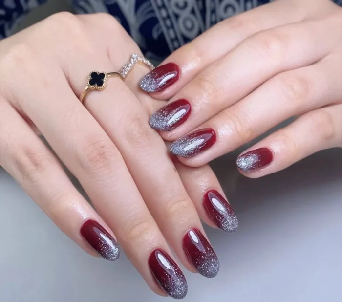 Oval nails with a glossy burgundy base featuring a sparkling silver glitter gradient fading from the tips.