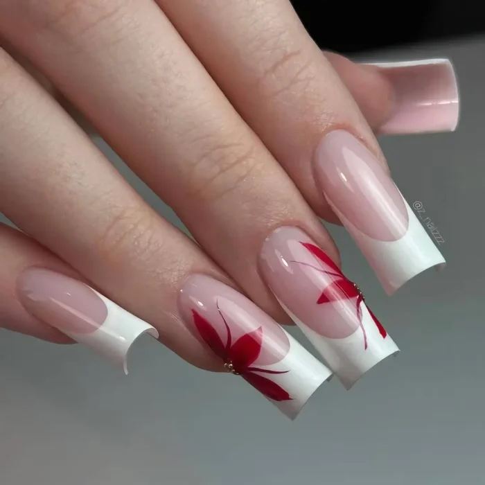 Square-shaped nails with a classic white French manicure, accented by abstract red floral designs and a gold stud.