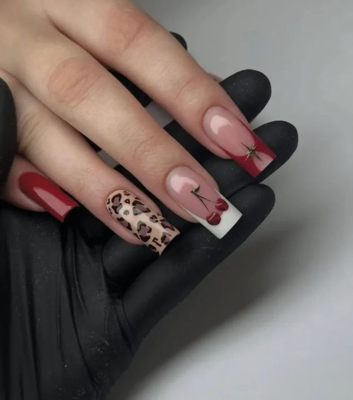 A bold mix-and-match red nail design featuring leopard print, cherry art on a white tip, and a red V-French with a star charm.
