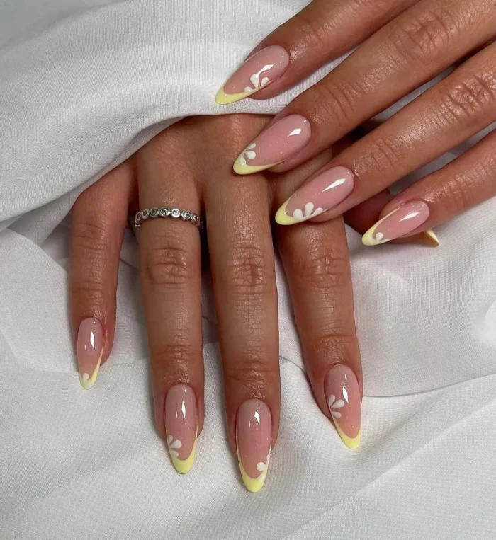 Elegant almond-shaped nails with sunny lemon yellow French tips, each featuring a delicate, stylized white five-petal flower accent.