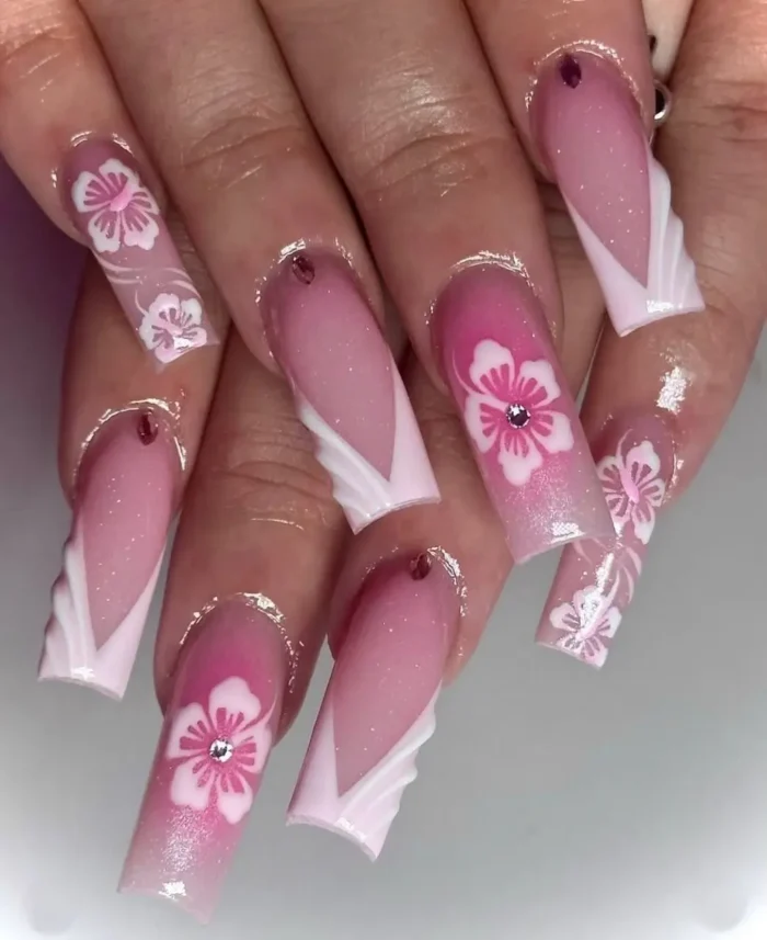 Long square nails with a shimmery pink ombré base, sharply angled white French tips, and hand-painted pink hibiscus flowers with rhinestone centers.