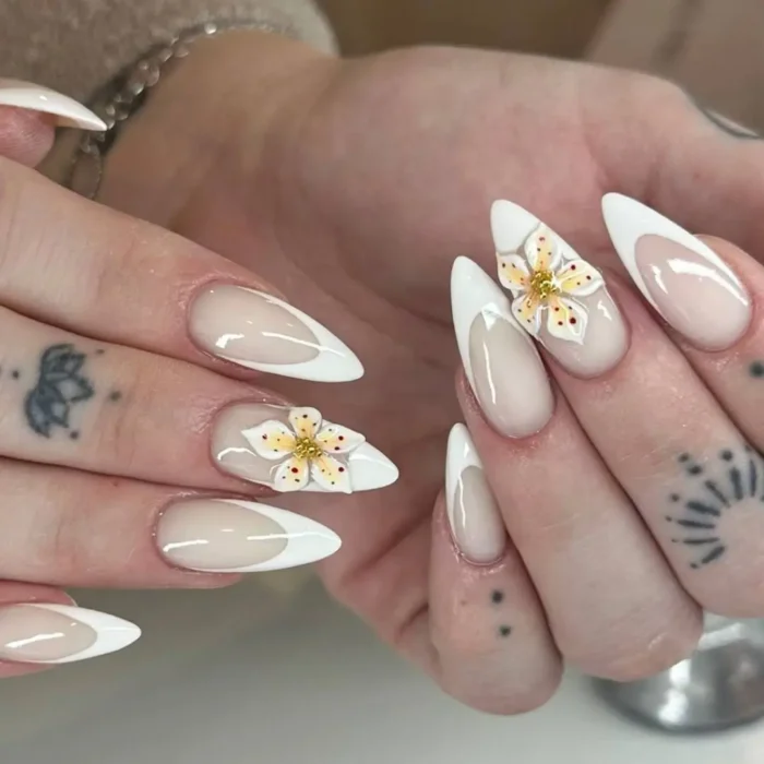 White French tip stiletto nails with a 3D white flower accent that has a yellow and orange speckled center.