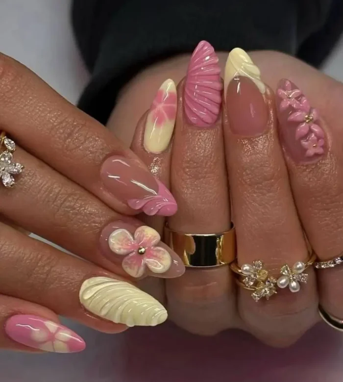 A vibrant and textured manicure with butter yellow and pink 3D floral designs, swirls, and seashell patterns.