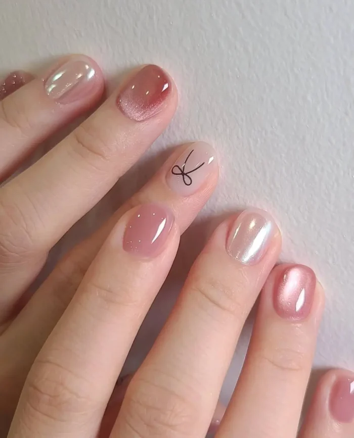 Cute simple gel manicure with rosy nudes, pearlescent shimmer, and a delicate black bow outline accent on short nails.