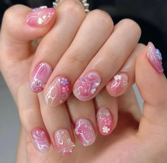 An intricate pink sakura-inspired nail art design with translucent layers, delicate white swirls, and 3D floral embellishments.