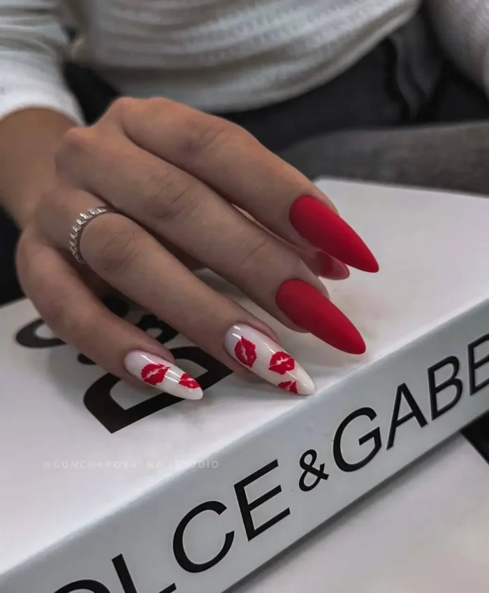 A playful red nail design with matte red stiletto nails and white accent nails covered in red lipstick kiss prints.