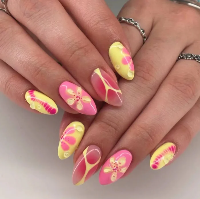 An artistic manicure with pink and butter yellow abstract floral patterns, color splashes, and 3D water droplet effects.