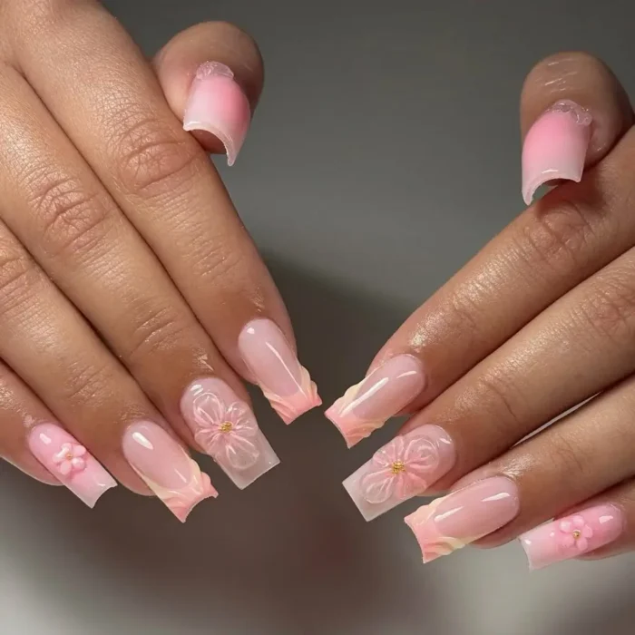 Long square-shaped nails with a milky nude base, pink ombré tips, and delicate 3D pink flower accents with gold bead centers.