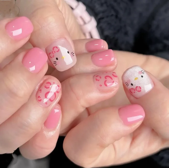 Short rounded nails with a cute pink theme featuring solid pink polish, character kitty faces with red bows, and sheer nails with red heart outlines.