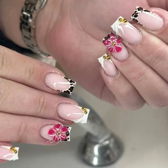 Square nails with a sheer nude base, white textured edges, gold metallic frames, and vibrant 3D pink flowers.