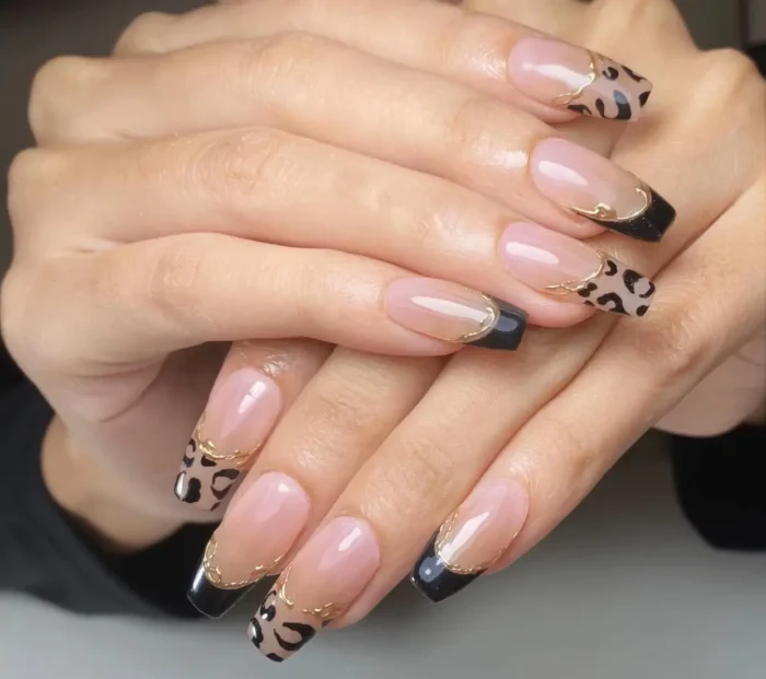 Long square nails with a modern French design featuring asymmetric tips with leopard print and solid black, divided by a wavy gold line.