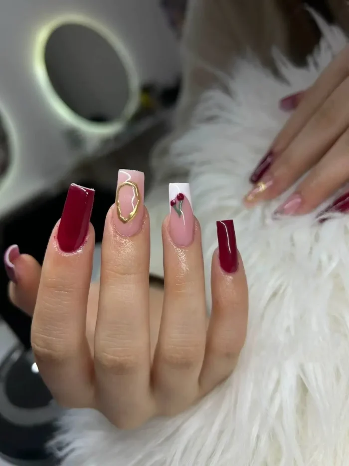 A sophisticated burgundy red nail design on square nails, with cherry and gold charm accent nails.