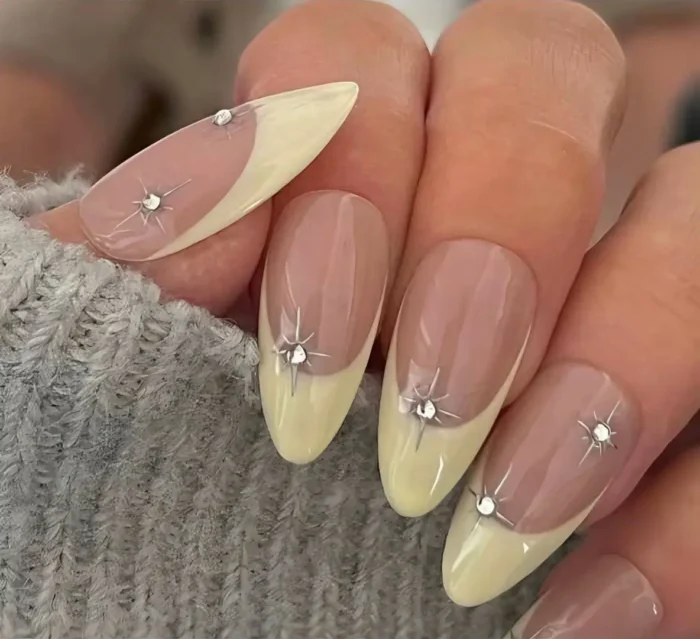 Butter yellow French manicure on almond nails accented with silver starburst and rhinestone details at the tip base.