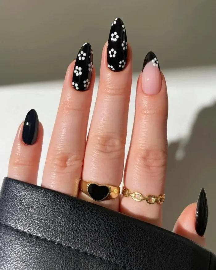 Almond-shaped nails with a mix of glossy black polish and accent nails with white daisy patterns on a black base.