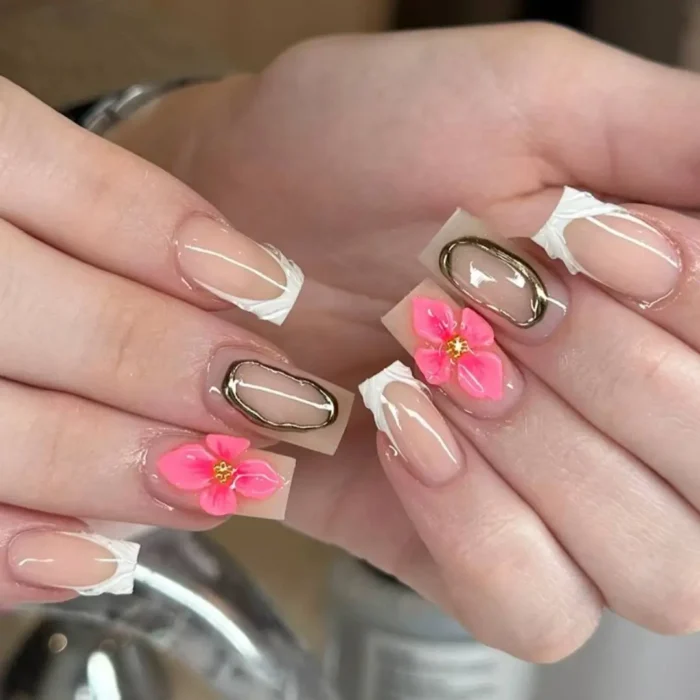 Square nails with a sheer nude base, abstract white tips, and vibrant 3D pink flowers framed by gold metallic accents.