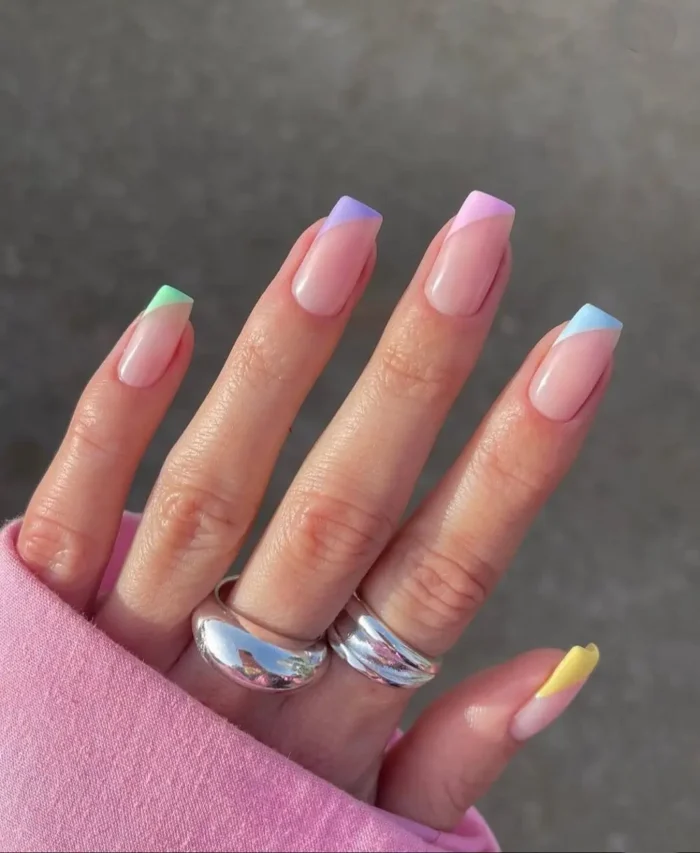 Nude nails featuring playful French tips in various soft pastel hues, adding a subtle pop of color.